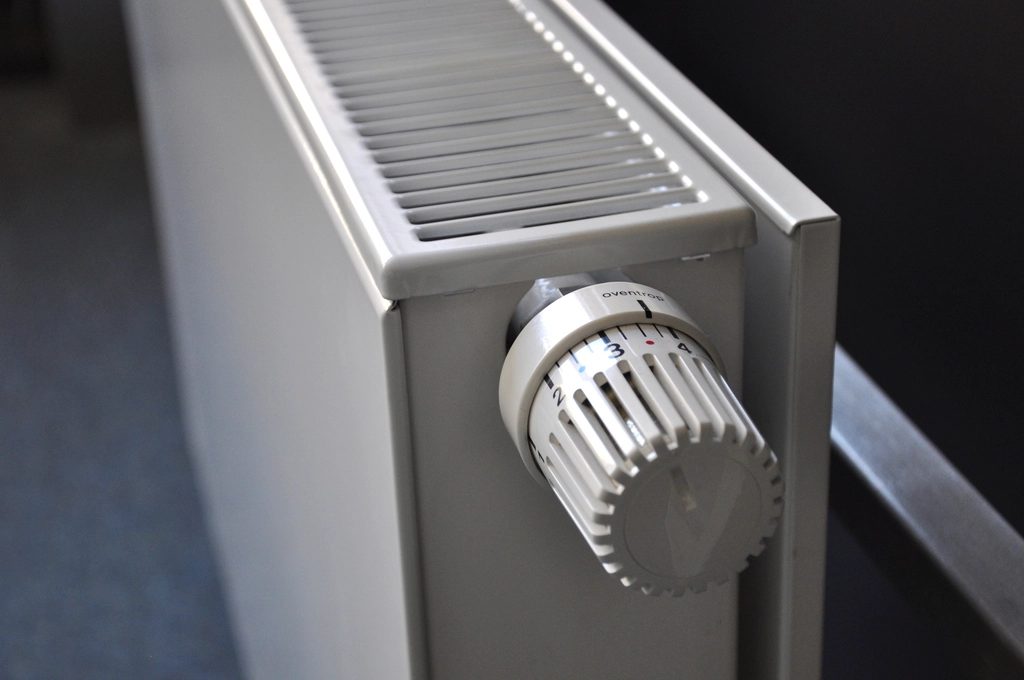 Witte paneelradiator met thermostaatknop aan de muur